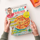 Titelblatt des Magazins „Iss dich GESUND“ mit Foto eines männlichen Erwachsenen in rotem Hemd links oben und einer großen Gemüsequiche in einer weißen Auflaufform darunter. Aufschriften: „Essen gegen Arthrose“, „Hilfe, Haarausfall!“, „Krank durchs Klima?“ und gelber Kreis mit „50 Kilo weniger“. Weiße Hintergrundfläche, Hände in grünem Strickpulli halten das Heft, orange Schale am oberen Bildrand.
