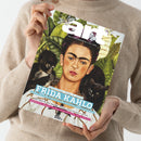 Person in beigefarbenem Strickpullover hält das Kunstmagazin „art – Das Kunstmagazin / Juli 2026“ in beiden Händen; das Cover zeigt ein Porträt von Frida Kahlo vor grünem Blätterhintergrund mit einem schwarzen Affen und einer schwarzen Katze. Sichtbare Texte: „FRIDA KAHLO“, „Jahrhundert-Schau in London“, „Die Poetik des Raums“, „Verrückte Genies? Ein Neurowissenschaftler über Kreativität“.