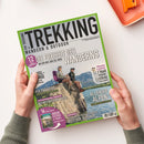 Titelblatt der Zeitschrift „Trekking – Wandern & Outdoor“ mit grünem Rand. Zentral zwei Personen mit Wanderausrüstung, Rucksäcken und Sonnenbrillen, sitzend auf einem Felsen vor Berg- und Seepanorama. Haupttitel „Die Freiheit des Wanderns“, weitere Texte: „Allgäuer Alpen“, „Norwegens raue Natur“, „Via Paradiso“ und „Green Outdoor & Travel“. Gehalten von zwei Händen über hellem Tisch mit orangefarbener Schale.