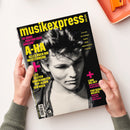 Hände halten ein Magazin mit schwarzem Cover und großem Schwarz-Weiß-Porträt einer männlichen Person in Lederjacke und T-Shirt. Gelbe Schrift mit Magazintitel „musikexpress“, Ausgabe „06/25“, Themen u. a.: „A-HA – Alles über ihr Meisterwerk“, „40 Jahre 'Hunting High and Low'“, „Lana Del Rey – Kaliforniens dunkle Königin“, sowie weitere gelb und pink gesetzte Überschriften zu Popkultur und Musik.
