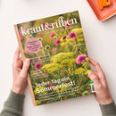 Titelbild der Zeitschrift „kraut&rüben – Schöner. Wilder. Biogarten.“ (Ausgabe 07/2026) mit Nahaufnahme blühender Sommerwiesenpflanzen in Gelb, Rosa und Grün. Aufschriften: „Tomatenliebe – Pflege-Leitfaden für köstliche Früchte“, „Griechisches Sein“, „Zukunftsspeicher“ und Haupttitel „Jeder Tag ein Sommerfest!“. Zwei Hände in grünem Strickärmel halten das Magazin über einer hellen Tischfläche.