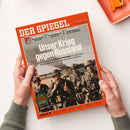 Titelseite des Magazins „Der Spiegel“ mit orangefarbenem Rand, schwarzem Logo und Foto von fünf Soldaten in Uniform und Helmen aus der Zeit des Zweiten Weltkriegs, im Hintergrund Rauch und zerstörte Landschaft. Hauptüberschrift: „Unser Krieg gegen Russland“. Untertitel thematisiert den Überfall von Nazi-Deutschland auf die Sowjetunion und dessen Nachwirkungen. In Händen einer Person mit grünem Strickpullover gehalten.