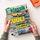 Titelblatt der Zeitschrift „Auto Bild klassik“ Ausgabe Juni 2025 mit grün-gelbem Design. Zentral ein gelber Mercedes 230 W123 auf grauer Straße, darunter kleinere Abbildungen von Ford Granada, Audi 100 LS, BMW 520, VW Passat B2 und Opel Commodore. Große Überschrift „Früher spießig, heute COOL“, gelber Balken „50 Jahre MANTA B“ und Textfeld „Wir starten zur JAPAN-CHALLENGE!“, gehalten von zwei Händen über hellem Tisch mit orangefarbenem Tablett.