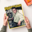 Magazin „Rolling Stone“ mit gelbem Rahmen und großem Titel in blauer Schrift; Cover zeigt eine männliche Person mit braunem Haar, gestreiftem hellgrünen Hemd und dunkler Hose, die an einer hellen Wand sitzt. Textaufschriften: „ELVIS“, „1956 – als Rock’n’Roll die Welt veränderte“, sowie kleinere Artikelhinweise zu Kim Gordon, Travis Scott und Noah Wyle. Magazin wird von zwei Händen über weißer Tischfläche gehalten, rechts eine orange Ablage.