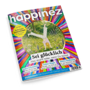 Titelbild des Mindstyle-Magazins „happinez“ mit bunter, kreisförmig strahlender Regenbogen-Illustration, in deren Mitte eine Person im Handstand auf grüner Wiese mit weißen Blumen und lila Blüten gezeigt wird. Sichtbare Texte: „Sei glücklich – Alles strahlt heller, wenn Du lachst“, „Selbst-Erkenntnis“, „Liebes-Magie“, „Aktive Hoffnung“, „Weiblichkeit – Die Superkraft Deines Zyklus“ sowie gelbes Etikett „Extra Zauberhafte Lesezeichen“.