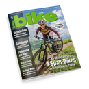 Titelblatt der Zeitschrift „bike“ Ausgabe 06/2023 mit großflächigem grün-blauem Schriftzug. Im Vordergrund eine weiblich gelesene Person mit Helm, Schutzbrille und Sportkleidung auf einem Mountainbike auf einem Waldweg. Im Hintergrund grüne Hügellandschaft unter blauem Himmel. Textausschnitte: „Vorsicht Fake!“, „Goldjunge“, „Elektronik am Bike“, „Watt-Training“, „Wechsel-Welle“, „All-Mountain-Test 4 Spaß-Bikes“ und „Dolomiten – die besten Touren im Felsental“.
