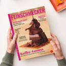 Titelbild der Zeitschrift „FEINSCHMECKER“ in Magenta-Schrift auf beigem Hintergrund, gehalten von zwei Händen. Zentrales Motiv: gestapelte Stücke dunkler Schokolade, übergossen mit flüssiger Schokolade. Sichtbare Überschriften: „SCHOKOLADE! Die Sieger des großen Tafel-Tests“, „Kaffee-Genuss“, „Südtirols Aufsteiger“, „Trendziel Tokio“ und „Schnitzel & Schmankerl“.