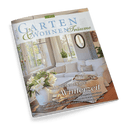 Titelbild der Zeitschrift „Garten & Wohnen Träume“, Ausgabe 1/2025, mit einem hell eingerichteten Wohnzimmer im Landhausstil: weiße Sofas, große Fenster, Spiegel, Holzelemente und Blumenarrangement in weißer Vase im Vordergrund; sichtbare Texte am unteren Rand u. a.: „Märchenhafte Winterzeit“, „Entspannt wohnen“, „Akzente im Garten“ und „Lebensart genießen“.