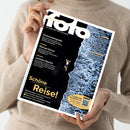 Person in beiger Strickkleidung hält das „fotoMAGAZIN“ (Ausgabe August 2023) vor neutralem Hintergrund. Auf dem Cover ist eine Luftaufnahme von einer männlichen Person am Rand einer felsigen Küste neben schäumendem Meer zu sehen, Titelzeilen u. a.: „Drohnenfotografie“, „Michael Kenna“, „Leichtes Gepäck“ und in großen gelben Buchstaben „Schöne Reise!“.