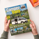Titelbild des Magazins „Camper Vans“ mit blau-gelbem Schriftzug, gehalten von zwei Händen über hellem Hintergrund. Auf dem Cover ein weißer Kastenwagen mit aufgeklapptem Dachzelt, vor grünem Wald; davor sitzt eine männliche Person auf einem Campingstuhl. Textüberschriften u. a.: „Der Kia kann’s!“, „Gasgrills getestet“, „Solartechnik“, „Rallye Dakar“, „Mieten in Florida“, „Laika Supremo 60“, „Geheimtipp Texel“.