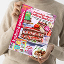 Eine hell gekleidete Person hält das Magazin „kochen & genießen“ mit pinkem Randstreifen und großformatigem Titelbild einer mehrschichtigen Schokoladen-Erdbeertorte. Aufschrift: „Traumhaft, diese Erdbeerkuchen!“, dazu kleinere Texte wie „Drei Gänge Spargel“, „Frühlingsleicht Neue Rouladen“ und „So flink gezaubert!“. Zusätzliche Elemente: gelber Hinweis „40 Jahre“, runde pinke Markierung und kleinere Rezeptbilder am unteren Rand.