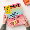 Magazintitel „ZEIT WISSEN“ in lila Schrift auf rosafarbenem Hintergrund, Untertitel „Bringt Sie auf gute Gedanken“. Gelber Kasten links mit Text „DER MOND – Die große Kraft am Himmel und ihr Einfluss auf die Menschen“. Haupttitel in schwarzer Schrift: „JETZT IST ERST MAL SOMMER – Wie man sich von Sorgen frei macht. Und neue Lebenslust gewinnt“. Titelillustration zeigt zwei Personen auf Liegestühlen am Strand mit Meer im Hintergrund.