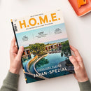 Titelblatt des Magazins „H.O.M.E. – Das Designmagazin zum Wohlfühlen“, Ausgabe August 2025, mit der Überschrift „Japan-Spezial“ und Untertitel „Signature Places“. Oben Themenzeilen: „Auf Schiene – Luxuszüge weltweit“, „Blended Travel – Arbeiten, wo andere Urlaub machen“ und „Neue Yachten – Wohnen auf dem Wasser“. Im Hintergrund ein modernes Resort mit Pool, Bäumen und flachen Gebäuden, gehalten von zwei Händen über hellem Tisch mit orangefarbenem Tablett.