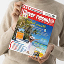 Helles Titelblatt des Reisemagazins „Clever reisen!“ mit rotem Schriftzug und gelber Überschrift „Urlaub perfekt – über 500 Insidertipps“, gehalten von einer Person in beigefarbenem Strickpullover. Im Hauptbild steht eine sommerlich gekleidete, weiblich gelesene Person mit weißem Hut und Kleid am tropischen Strand mit Palmen. Weitere sichtbare Texte: „Special Deutschland“, „Mehr erleben“, „Unsere Lieblingsziele am Mittelmeer“.