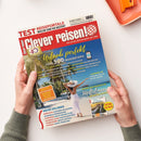 Titelseite des Reisemagazins „Clever reisen!“ in rotem Schriftzug mit weißem Hintergrund; Hauptüberschrift „Urlaub perfekt – über 500 Insidertipps“. Eine Person in weißem Sommerkleid und Hut steht mit ausgebreiteten Armen am Strand unter Palmen. Weitere Texte: „Special Deutschland“, „Unsere Lieblingsziele am Mittelmeer“ und „Extra im Heft: Flusskreuzfahrten“. Gehalten von zwei Händen vor hellem Hintergrund.