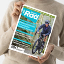 Person in beigefarbenem Pullover hält ein Magazin mit dem Titel „Elektro Rad“. Auf dem Cover ist eine lächelnde, fahrradfahrende Person mit Helm, Sonnenbrille und dunkler Kleidung auf einem Schotterweg zu sehen. Textaufschriften: „Flotter auf Schotter – 11 Gravelbikes mit Spaß-Garantie“, „Der perfekte Sattel! Darauf kommt es an!“, „Rushhour: Tipps vom Verkehrs-Experten“, „Eurobike-Neuheiten: Das Beste von der Messe“.