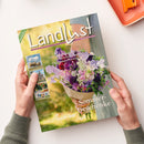 Magazin „Landlust“ mit Titeltext „Sommer-Geschenke“ in weißen Buchstaben, gehalten von einer Person mit hellgrünem Pullover über hellem Tisch. Auf dem Cover ein Strauß aus lila, rosa und weißen Blumen vor verschwommenem Gartenhintergrund; zusätzliche Texte: „Selbst gebaut: Pflanzkasten für Kräuter“, „Fruchtig: Kuchen ohne Backen“, „Rothirsch: Anbauen und ernten“. Linker Rand mit kleinen Fotos von Tieren, Haus und Gartenmotiven.
