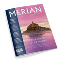 Magazin „MERIAN – The Art of Travel“ mit Titelmotiv einer beleuchteten Klosteranlage auf einer Felseninsel in der Abenddämmerung. Schriftzüge: „JENSEITS VON PARIS – Frankreichs Norden neu entdeckt“, Themen im linken blauen Rand u. a. „Magischer Oman“, „Viva Valencia!“, „Legendäre Hotelbars“, „Bodensee“. Unten Logo „Mit Google Maps Service“ sowie Ausgabe- und Preishinweise klein gedruckt.