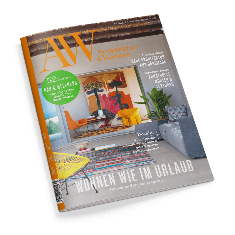 Titelbild der Zeitschrift „AW Architektur & Wohnen“ mit dem Haupttitel „Wohnen wie im Urlaub – Häuser an Sehnsuchtsorten“; im Vordergrund ein modernes Wohnzimmer mit bunter Einrichtung, darunter ein gestreifter Teppich, gelber Stuhl, graues Sofa, Pflanzen und farbige Wandkunst; sichtbare Schlagzeilen: „52 Seiten Bad & Wellness“, „Neue Architektur aus Dänemark“, „Kunstvolle Muster & Texturen“ und ein Dossier zu KI im Design.