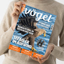 Person in beigem Strickpullover hält das Magazin „Vögel – Magazin für Vogelbeobachtung“, Ausgabe Nr. 87–5/2025, mit einem Titelbild eines fliegenden Seeadlers über Wasser. Aufschriften: „Vögel am Bodensee – Beobachtung im Eriskircher Ried“, „König der Lüfte – Seeadler im Aufwind“, „Stunde der Gartenvögel“, „Im Test: Fernglas Zeiss SFL 8x40 – Größer, kompakter, leichter“, „Erforscht“, „Bestimmt“, „Aufgedeckt“.