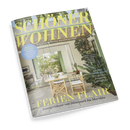 Magazincover der Zeitschrift „Schöner Wohnen“ mit großem gelbem Schriftzug, Untertitel „Europas größtes Wohnmagazin“. Abgebildeter Innenraum mit offener Terrasse, Holztisch, zwei Stühlen, grünen Fensterläden und großen Zimmerpflanzen. Textausschnitte u. a.: „Ferien-Flair – Sommerhäuser von Dänemark bis Marokko“, „Outdoor-Tipps“, „Komfort-Zone“ und „An der Garden Route“.