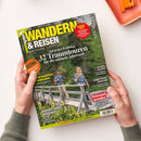 Titelbild des Magazins „Wandern & Reisen“ Ausgabe 02-25 Frühling, gehalten von zwei Händen über hellem Hintergrund. Auf dem Cover ein Foto von einer weiblichen und einer männlichen Person mit Rucksäcken auf einer Holzbrücke in grüner Waldlandschaft. Sichtbare Texte: „32 Traumtouren“, „Steiermark genießen“, „Ausrüstungsratgeber“, „Gewinnspiel“ und „Ursprüngliches Graubünden“. Farbtöne: Grün, Gelb, Weiß und Rot.