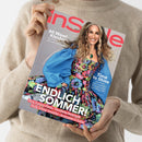 Person in beigefarbenem Pullover hält das Magazin „InStyle“. Auf dem Cover eine weibliche Person mit langen, gelockten Haaren in einem bunten, floralen Kleid mit blauer Jacke, lächelnd vor grauem Hintergrund. Sichtbare Texte: „60 Wow!-Kleider – Vom Partyknaller bis zum Office-Hit“, „Time to Shine“, „ENDLICH SOMMER!“, „Flirty Fransen-Pieces – Trendfarbe Buttergelb – Heiße Schnür-Sandalen – Accessoires in Sorbet“.