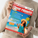 Person mit beigem Pullover hält das Magazin „Clever reisen!“ mit rotem Titelkopf und weißer Schrift, Unterzeile „Reise-Insider seit 1986“. Auf dem Cover eine lächelnde weibliche Person in türkisfarbenem Kleid und Strohhut an einem Sandstrand mit Meer und Palmen. Sichtbare Schlagzeilen zu Reisetipps, Spanienurlaub und Gewinnspiel „Insel Poel“, Hauptfarben Rot, Blau und Gelb, Aufmachung im Hochglanzstil.