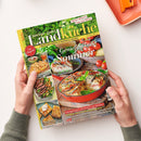 Titelblatt der Zeitschrift „meine gute Landküche“ mit grün-gelbem Schriftzug und Untertitel „Ländlicher Genuss & regionale Vielfalt“, Ausgabe Juli/August 2016. Im Mittelpunkt eine runde Gemüse-Quiche in roter Form, daneben Tomaten und Kräuter. Weitere Abbildungen zeigen Brot, Steaks und Kuchenstücke. Textelemente u. a.: „Genießen im Sommer“, „Hausgemacht schmeckt’s am besten!“, „Das Original“. Gehaltene Zeitschrift in zwei Händen vor hellem Hintergrund.