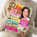 Frau in beigefarbenem Strickpullover hält das bunte Magazin „Lisa“ mit gelbem Rand und rotem Titel; auf dem Cover rechts ein Porträt einer lächelnden Frau, links Texte und Fotos zu Themen wie „Kuchenträume mit Himbeeren“, „Abnehmspritze“, „Outdoor-Glück“, „Hunger-Stopper“ und „Mode-Liebling T-Shirt“, ergänzt durch kleinere Bilder von Kuchen, Möbeln und Kleidung auf hellem Hintergrund.