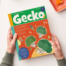 Titelblatt der Kinderzeitschrift „Gecko“ in den Farben Grün, Orange und Gelb, gehalten von zwei Händen vor hellem Hintergrund. Oben großes grünes Logo „Gecko“, darunter farbige Illustrationen von drei Brokkoli-Figuren in weißen Raumanzügen im All. Aufdrucke: „PIZZA Sechs Jahreszeiten“, „JUPP und die Gemüsesägung“, „BROKKOLI im All“ sowie Hinweis auf Geschichten- und Sprachspiele zum Thema Gemüse.