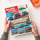 Titelbild der Zeitschrift „auto motor und sport“, gehalten von zwei Händen über hellbeigem Tisch. Auf dem Cover große Überschrift „Einsteiger zum Aufsteigen“ über einem Foto von drei fahrenden Autos (Mercedes, Audi, BMW) auf einer Straße. Weitere kleinere Fahrzeugbilder darunter mit Texten wie „10 neue schon gefahren“ und Hinweisen auf Artikel zu Porsche, VW, Renault und Mercedes. Oben links rotes Logo-Feld mit weißem Schriftzug.