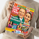 Person in beigefarbenem Strickpullover hält das Magazin „Echo der Frau“. Titel in weißer Schrift auf rotem Hintergrund, Hauptüberschrift: „Traum-Hochzeit im Mai“. Darunter mehrere kleinere Schlagzeilen über Prominente wie „Anita Hofmann & Christian – Jetzt ein süßes Baby!“ und „König Carl Gustaf – Silvia macht ihm das schönste Geschenk“. Bunt gestaltetes Cover mit Fotos mehrerer Personen vor gelbem, blauem und rotem Hintergrund.