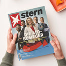 Titelblatt des Magazins „stern“ mit fünf Personen in halbnaher Aufnahme vor blauem Hintergrund, mittig eine Person in rotem Blazer, darüber großes weißes Logo „stern“ mit weißem Sternsymbol und der Titelaufschrift „DIE AFD-BESIEGER“. Darunter gelber Untertitel sowie weitere Textzeilen in Weiß und Blau zu Themen wie „Ein Jahr Papst“ und „Sozialgeldbetrug“. Hände halten das Magazin über hellem Tisch mit orangefarbenem Tablett.