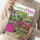 Helle, langärmlig gekleidete Person hält das Magazin „GartenFlora“ Ausgabe Juni 2025 in beiden Händen; Titelbild zeigt einen üppigen Garten mit pinken und weißen Rosenblüten, oben links ein Foto mit Sukkulenten in Töpfen. Sichtbare Texte: „gärtnern, erleben und genießen“, „Die Besten für den Garten – Duftrosen“, „Pflegeleichte Trocken­künstler“, „Rasenmäher mit Akku-Antrieb“, weitere Themen in rosafarbenem Kasten unten links.