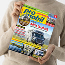 Person mit beigem Strickpullover hält die Zeitschrift „promobil“ Ausgabe Juni 2023 in beiden Händen; auf dem Cover ein silbernes Reisemobil Mercedes‑Benz Adria Coral MB auf einer Landstraße, dazu Titelzeilen u. a.: „Transit mit Allrad – Der Sunlight 4x4 im Dauertest“, „Hilfe, es brennt“, „Adria Coral MB – schick und modern“, „Campen am Wasser“ und „Mehr Zuladung – Leichtbau, aber solide“, mit gelb‑blauer Kopfzeile und rotem Preisfeld oben rechts.
