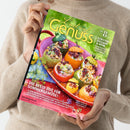 Person mit beigefarbenem Strickpullover hält das Magazin „Lust auf Genuss“ no. 8 in der Hand, Titel in gelber Schrift auf grünem Hintergrund. Auf dem Cover ist eine rote Schale mit gefüllten Zucchini, Paprika und Tomaten in Gelb, Grün und Rot zu sehen. Text: „DIE BESTE ZEIT FÜR SOMMERGEMÜSE!“ und „TOMATEN ZUCCHINI & MEHR – köstlich-kreativ kombiniert mit Fleisch & Fisch“.