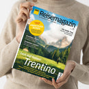 Helle, langärmlig gekleidete Person hält das „ADAC Reisemagazin“ mit Titelbild einer Berglandschaft mit grüner Wiese, Nadelbäumen und Felsgipfeln unter leicht bewölktem Himmel. Sichtbare Texte: „14 Seiten Extra Abenteuer-Reisen“, „Kroatiens Inseln“, „Schweden erleben“, „City-Guide: Prag“, sowie Haupttitel „Lust auf Italien! Trentino – Geheimtipp zwischen Alpen und Gardasee“.