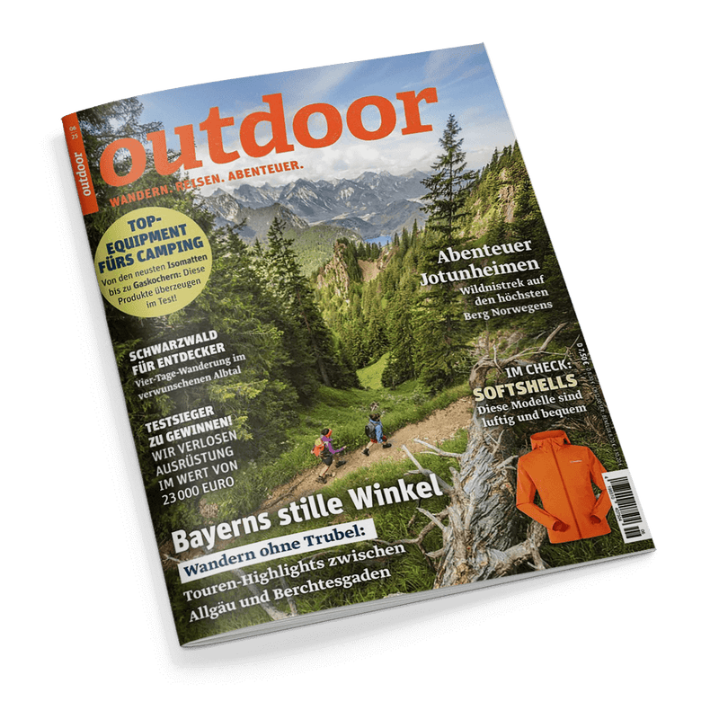 Titelbild der Zeitschrift „outdoor – Wandern. Reisen. Abenteuer.“ mit großem orangefarbenem Schriftzug vor Alpenpanorama; im Vordergrund drei wandernde Personen auf schmalem Gebirgspfad durch grüne Berglandschaft. Sichtbare Textelemente: „Bayerns stille Winkel“, „Abenteuer Jotunheimen“, „TOP-EQUIPMENT FÜRS CAMPING“, „IM CHECK: SOFTSHELLS“, daneben ein orangefarbener Softshell-Mantel und ein Barcode am rechten unteren Rand.
