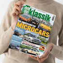 Person mit beigefarbenem Wollpullover hält eine Ausgabe der Zeitschrift „Auto Bild Klassik“ in beiden Händen, Titelthema „Die unbekannten Microcars“. Auf dem Cover sind mehrere klassische Autos in verschiedenen Farben (orange, schwarz, gelb, silbern) aus Frontal- und Schrägperspektive zu sehen sowie Überschriften zu weiteren Artikeln, etwa über den Opel Manta 400, Mercedes 190 E 2.0 und das W123 Challenge-Logo unten rechts.