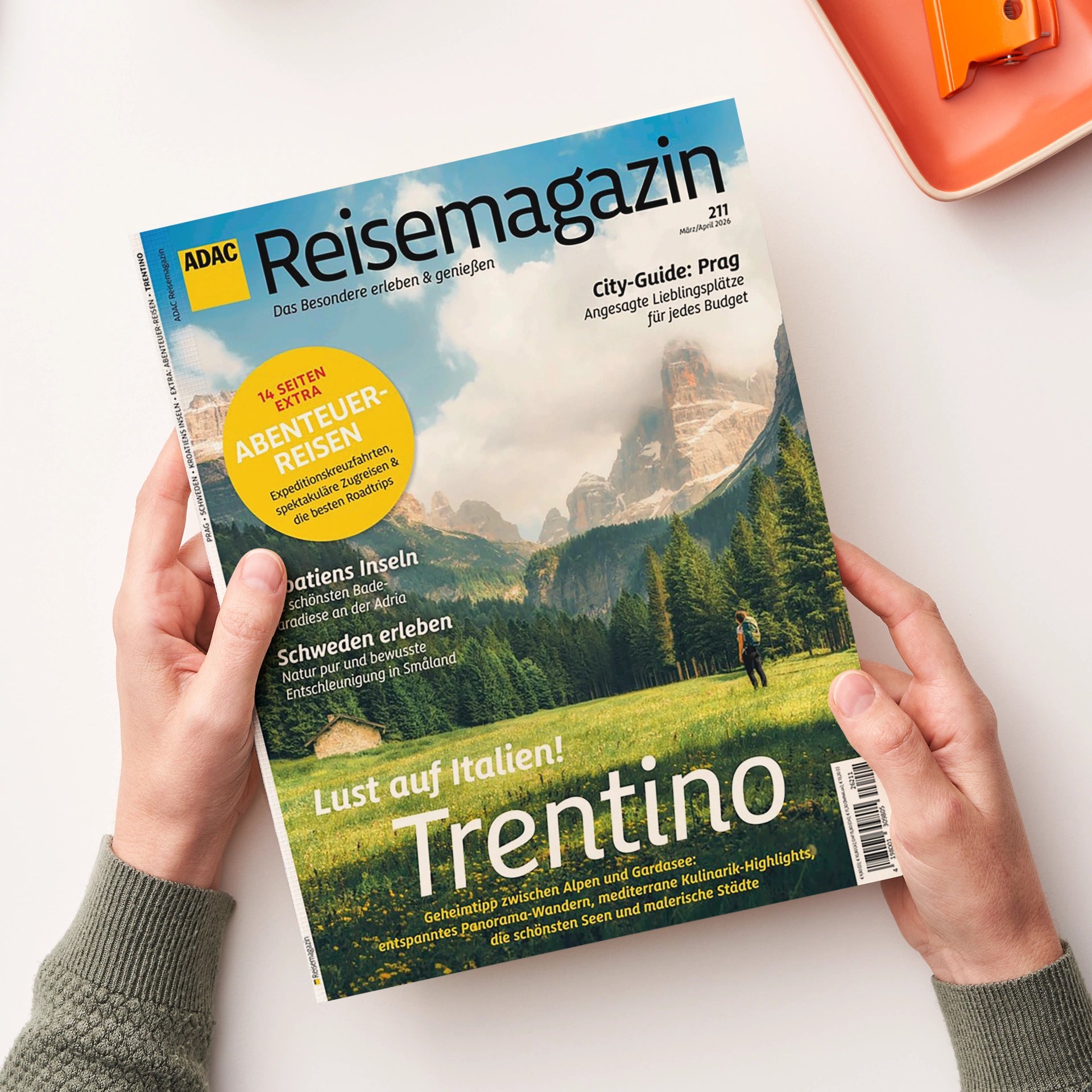 Titelblatt des „ADAC Reisemagazins“ mit der Überschrift „Lust auf Italien! Trentino“, Unterzeilen zu Kroatien, Schweden und Prag sowie einem gelben Kreis mit dem Text „14 Seiten Extra Abenteurreisen“. Das Cover zeigt eine Berglandschaft mit grüner Wiese, Bäumen und einer wandernden Person im Vordergrund, im Hintergrund graue Felsgipfel unter leicht bewölktem Himmel, gehalten in natürlichen Grün- und Brauntönen.