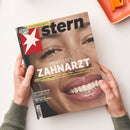 Titelblatt des Magazins „stern“ mit großem Porträt einer lächelnden, weiblich gelesenen Person mit Sommersprossen, Fokus auf Zähne und Gesicht. Oben links rotes Stern-Logo mit weißem Sternsymbol. Hauptüberschrift „Praxistest Zahnarzt“ in weißen Großbuchstaben, weitere Textelemente: „Der große stern-Report“, „Katherina Reiche“, „Russlands Epstein-Skandal“ und Hinweis auf „Fußball WM 2026“. Hände halten das Magazin vor hellem Hintergrund.