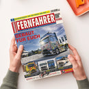 Titelbild der Zeitschrift „Fernfahrer – Das Truck-Magazin für Berufskraftfahrer“, gehalten von zwei Händen auf hellem Tischhintergrund. Im oberen Bereich roter Schriftzug „FERNFAHRER“ auf weißem Balken, darunter blauer Untertitel. Zentrales Motiv: bunt lackierter Lkw vor Gebäuden und Fahnen bei Tageslicht, umgeben von kleineren Bildern weiterer Lastwagen; Schlagzeilen u. a. „GEBAUT FÜR EUCH“ und „GETRAGEN VON EUREM VERTRAUEN“.