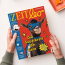 Titelblatt des Kindermagazins „ZEIT Leo“ mit rotem Hintergrund, zentraler Abbildung einer Ziege mit blauer Superheldenmaske und Umhang. Gelber Schriftzug „Die Superkraft der Tiere“, daneben gelber Stern mit Text „So machen dich Ziege, Huhn und Hase stark“. Linke blaue Randspalte mit weißem „Greg“-Comicgesicht und Überschriften zu Themen wie „WM-Stars“, „Spurensuche“ und „Tempo 300“. Zwei Hände halten das Heft über hellem Tisch.