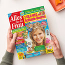 Buntes Cover der Zeitschrift „Alles für die Frau“, schräg von oben fotografiert und von zwei Händen gehalten. Darauf eine lächelnde blonde Frau sowie die Texte „3 KILO WEG mit Schlank-Beeren“, „Kostenfallen entlarven“, „Sparen Sie über 300 Euro im Alltag!“, „Stoppen sofort den Heißhunger“, „Super-Wochenplaner“ und „Riesen-Rätsel-Spaß“.