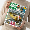 Hände einer Person im beigefarbenen Strickpullover halten schräg eine Zeitschrift mit grün-weißem Titel „Angel Woche“ und der Aufschrift „Deutsche Sportfischer Zeitung“. Das Cover zeigt mehrere Fische im Wasser sowie Texte wie „Das große Fressen!“, „Spinnrolle Cardiff XR C2000S von Shimano“, „Frage der Woche“ und „Mit ANGELSEE“.