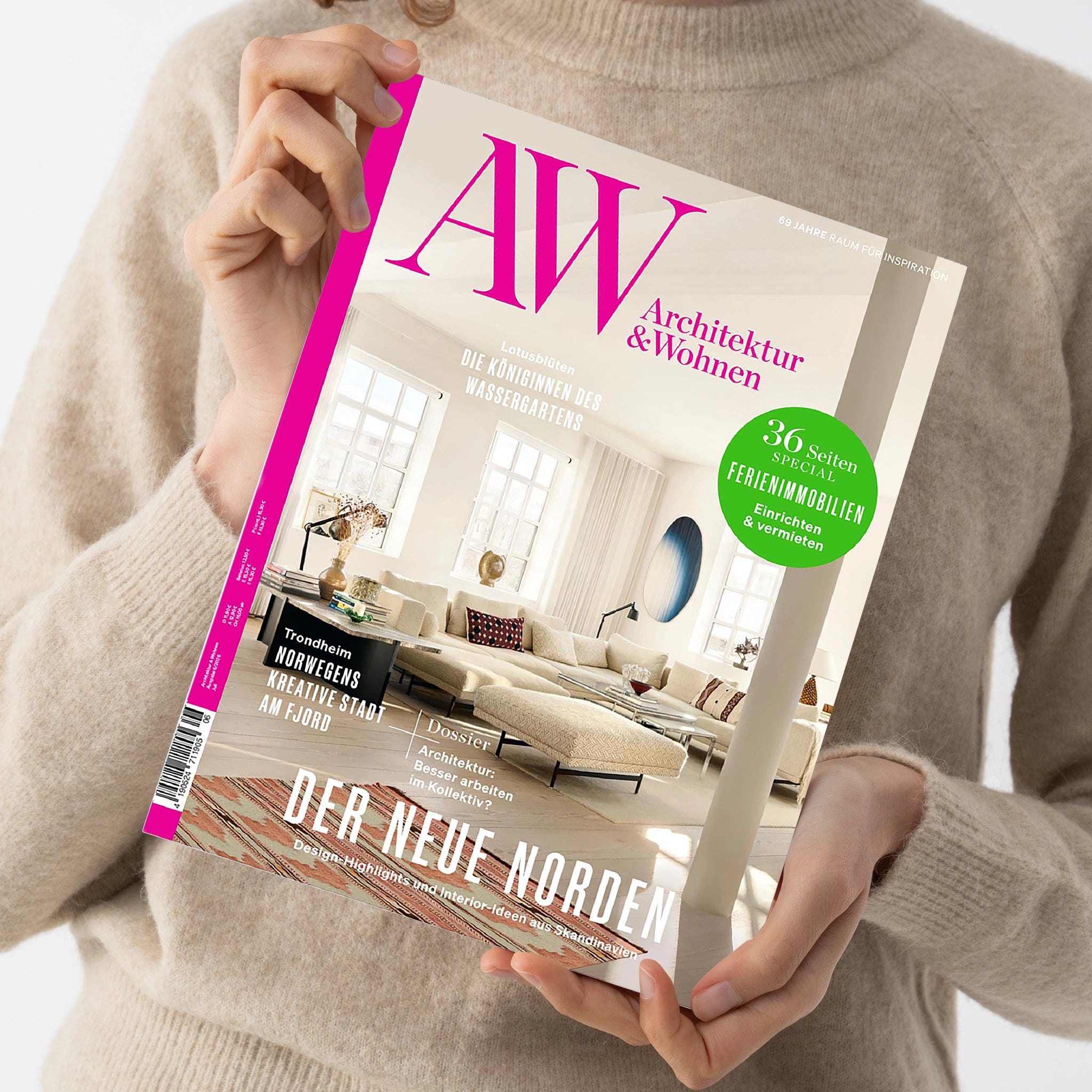 Weibliche Person im beigefarbenen Strickpullover hält eine schräg fotografierte, cremefarbene Zeitschrift mit pinkem Rand und Wohnraumfoto auf dem Cover. Sichtbare Texte: „AW“, „Architektur & Wohnen“, „69 Jahre Raum für Inspiration“, „36 Seiten Special Ferienimmobilien“, „Der neue Norden“ sowie „Design-Highlights und Interior-Ideen aus Skandinavien“.