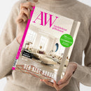 Weibliche Person im beigefarbenen Strickpullover hält eine schräg fotografierte, cremefarbene Zeitschrift mit pinkem Rand und Wohnraumfoto auf dem Cover. Sichtbare Texte: „AW“, „Architektur & Wohnen“, „69 Jahre Raum für Inspiration“, „36 Seiten Special Ferienimmobilien“, „Der neue Norden“ sowie „Design-Highlights und Interior-Ideen aus Skandinavien“.