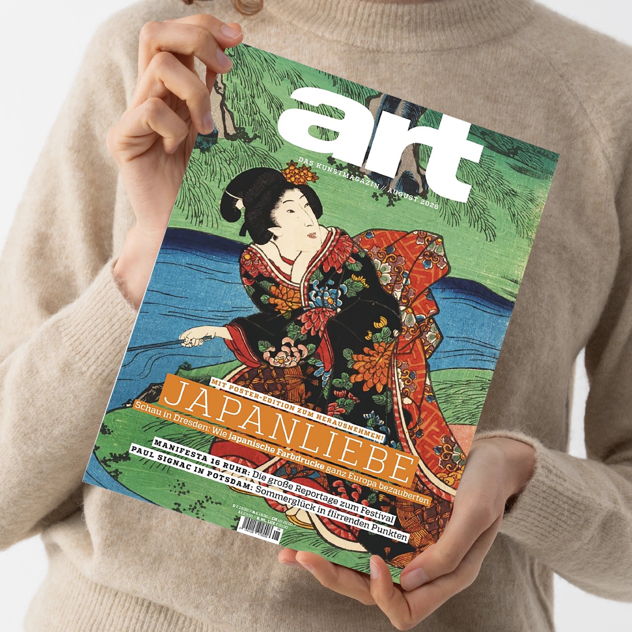 Kunstmagazin „G...“ mit grün-blauem Cover und japanischer Holzschnittdarstellung einer Frau im floral gemusterten Kimono, gehalten von einer Person im hellbeigen Strickpullover. Sichtbare Texte: „DAS KUNSTMAGAZIN/AUGUST 2026“, „JAPAN LIEBE“, „MIT POSTER-EDITION ZUM HERAUSNEHMEN!“, „MANIFESTA 16 RUHR“ und „PAUL SIGNAC IN POTSDAM“.