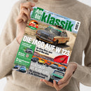 Eine Person im beigefarbenen Strickpullover hält schräg eine Ausgabe des Automagazins „Auto Bild Klassik“. Das Cover zeigt einen Mercedes-Benz W123 vor einer Wüstenlandschaft sowie weitere klassische Fahrzeuge und eine marokkanische Flagge; lesbare Texte sind „W123 Challenge“, „Die Jagd auf W123“, „Lastentier mit Leidenschaft“, „Im alten Benz quer durch Marokko“ und „Klassiker bis 10.000 Euro“.